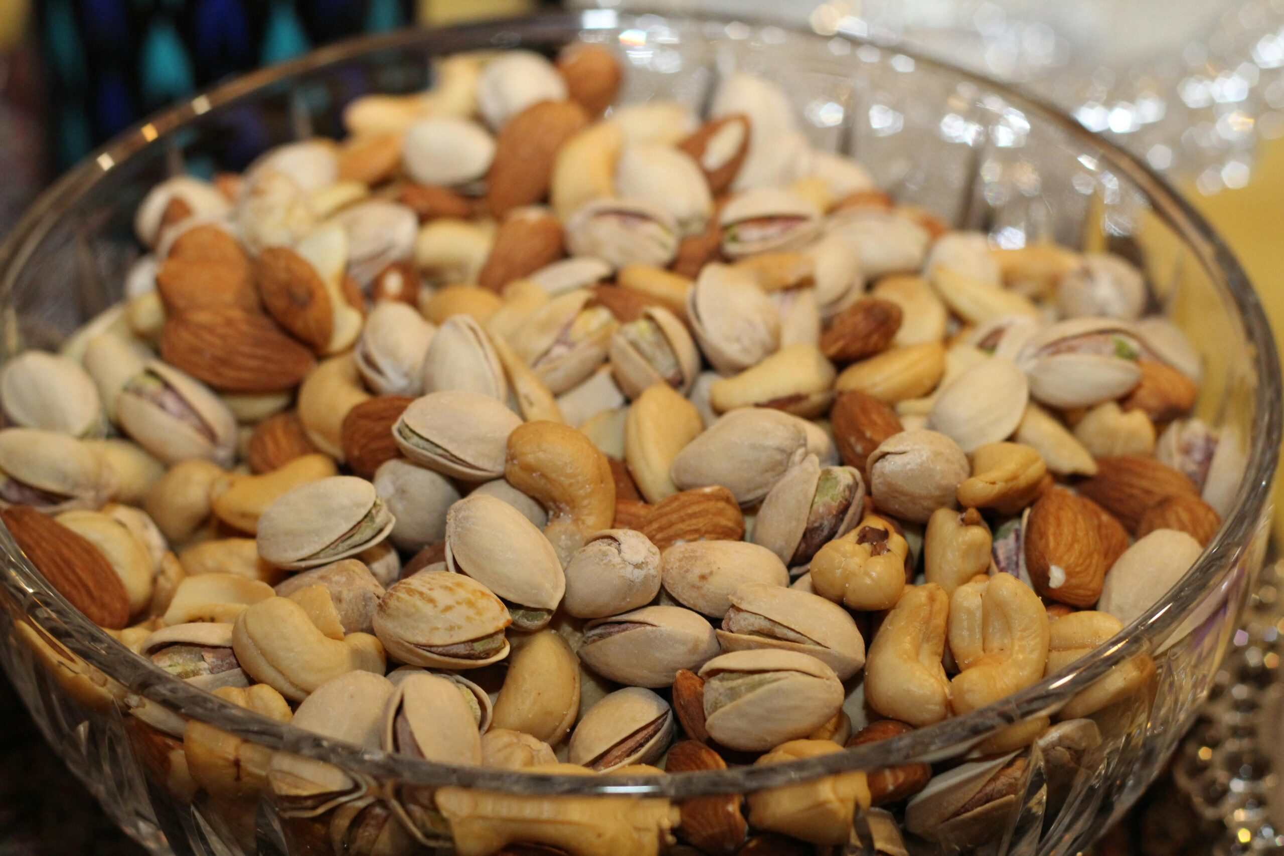 A close-up view of a glass bowl filled with various mixed nuts, including almonds, cashews, and pistachios.